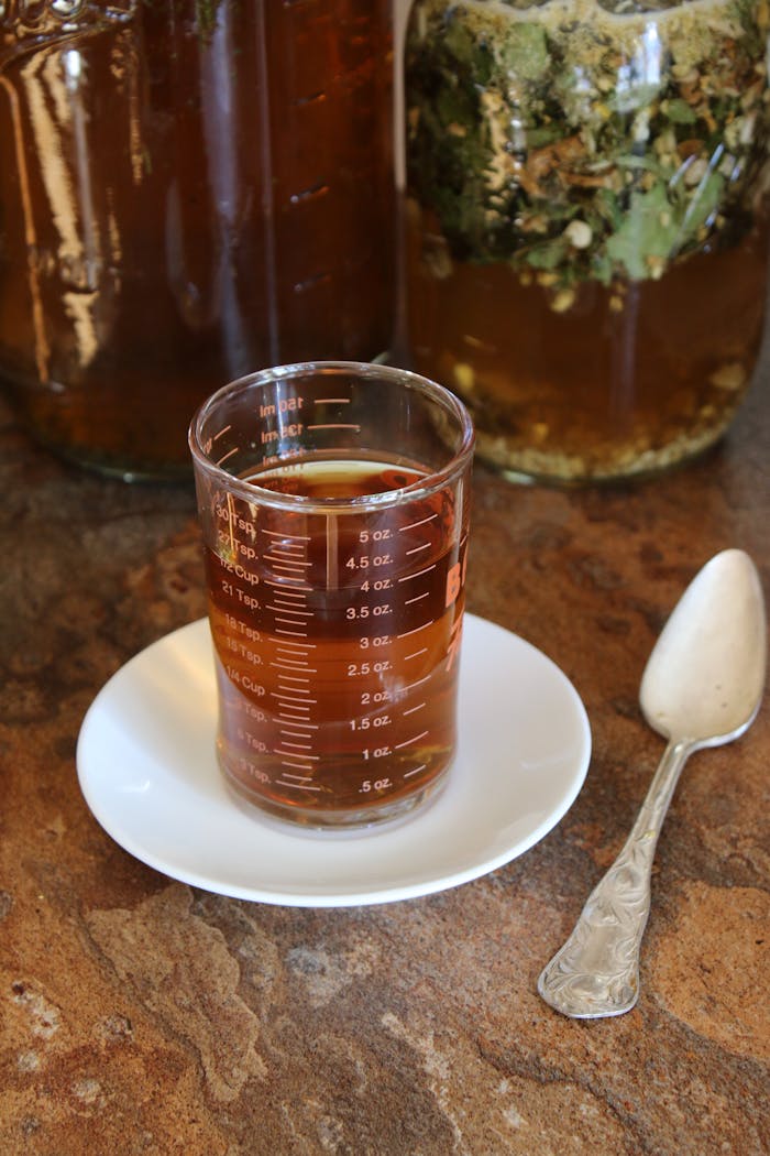 Aromatic herbal tea in a measurement glass on a saucer with jars in background.