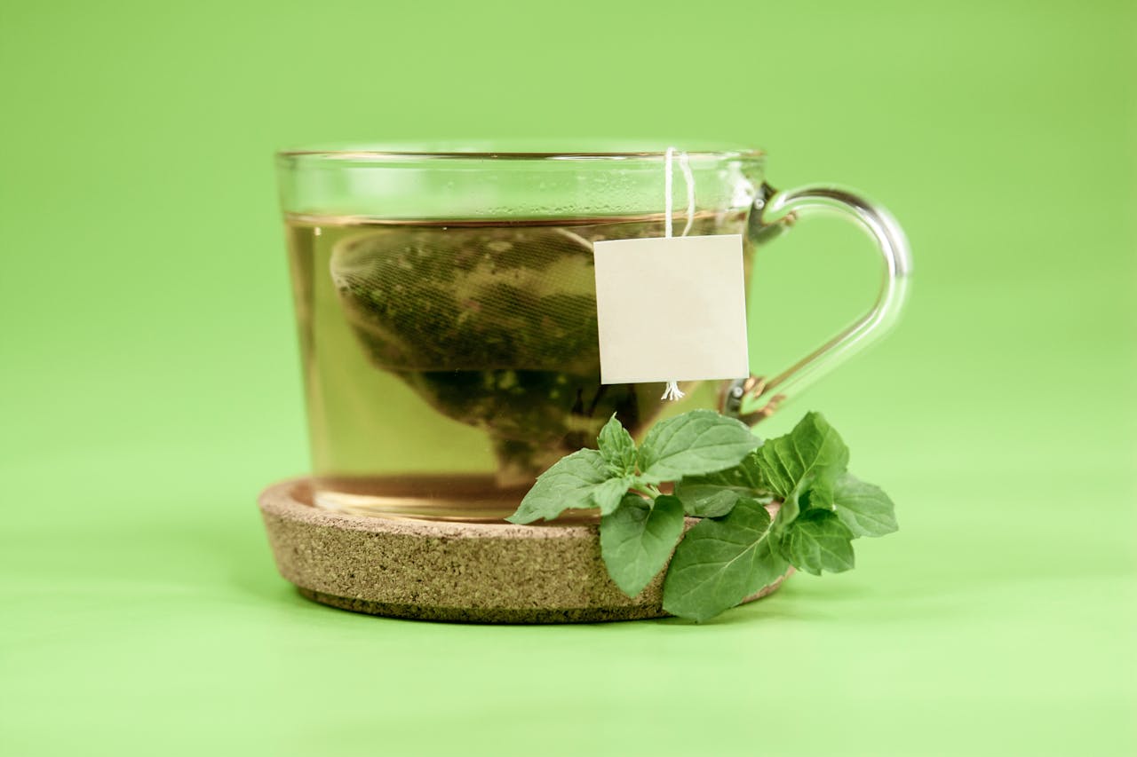 services-img Green tea bag in glass cup with hot water on cup holder with mint leaves placed on green background